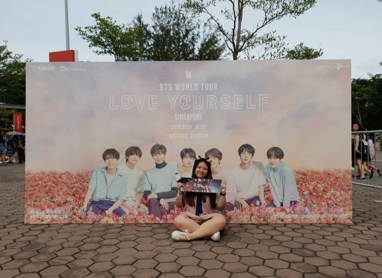 A photo of K-pop fan Tan Li En posing in front of a BTS World Tour banner at BTS' 2019 live concert in Singapore