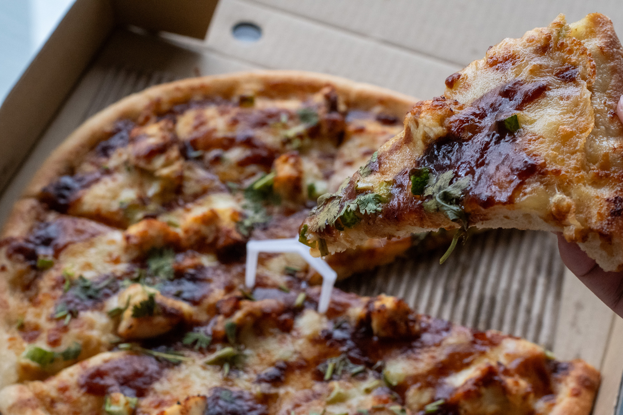 The pizza is topped with marinated chicken, cucumber, sweet sauce, and coriander.